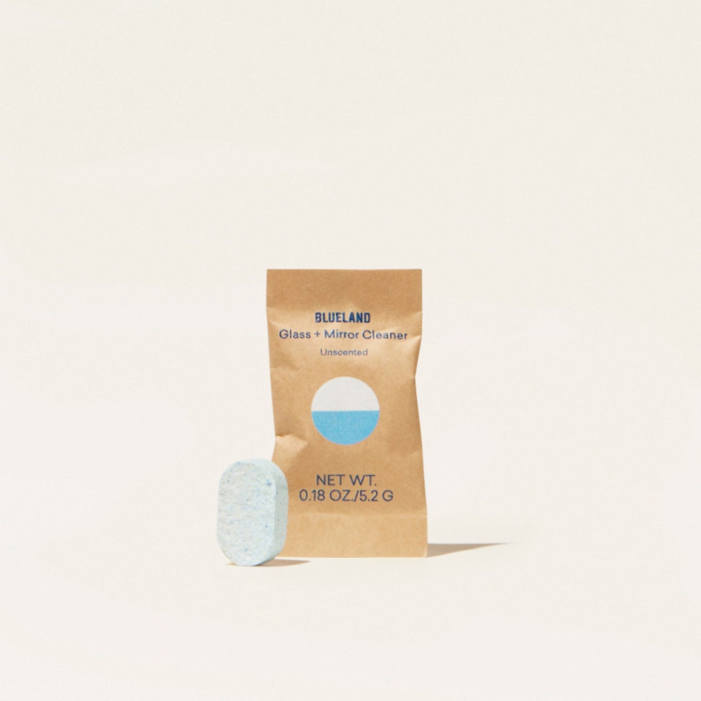 A small blue tablet stands beside a brown packet labeled Glass + Mirror Cleaner Tablet Refills, Unscented with a blue circle, net weight 0.18 oz (5.2 g). This plant-powered cleaner uses refill tablets and is set against an off-white background.