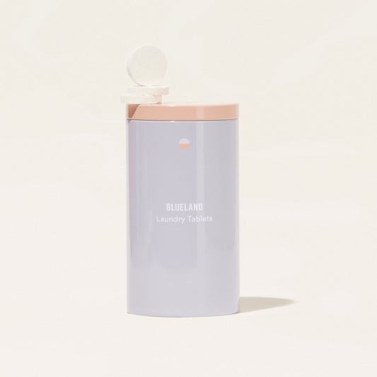 A cylindrical Blueland Laundry Detergent Starter Set (Bundle) with a pale pink lid is shown. One plant-based cleaning tablet sits on the open lid, emphasizing these plastic-free tablets against a light, neutral background.