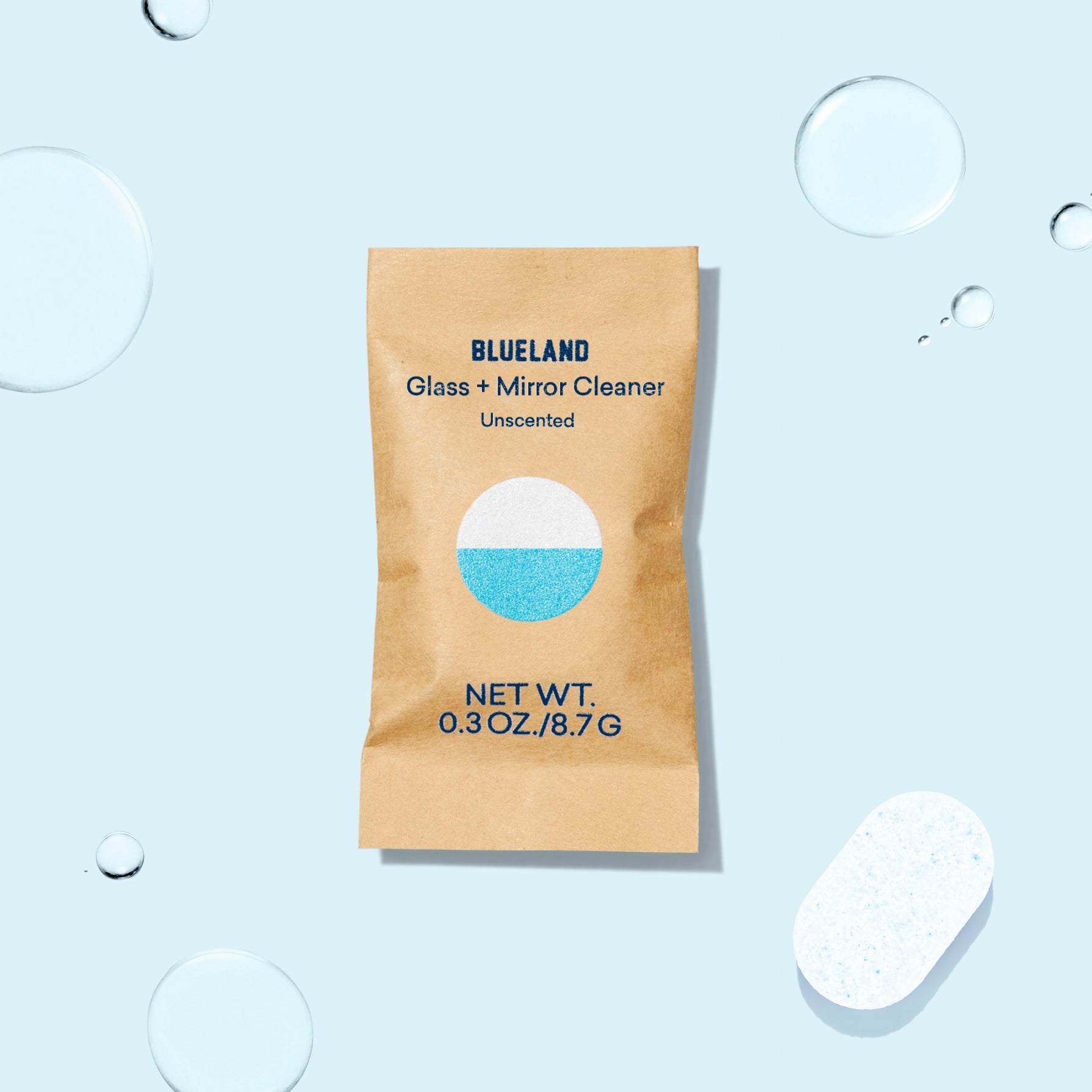 A beige packet of Glass + Mirror Cleaner Tablet Refills, labeled Unscented and Net Wt. 0.3 oz/8.7 g, sits against a light blue background with water droplets and refill tablets, highlighting a plant-powered cleaner for streak-free shine.
