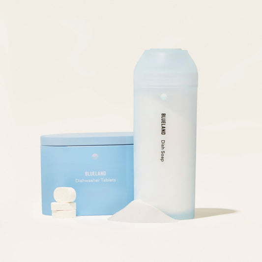 A blue Dish Duo container with Blueland Dishwasher Tablets alongside three white eco-friendly tablets and a tall translucent Dish Duo bottle of Blueland Dish Soap featuring plant-based ingredients, with a pile of white powder in front.